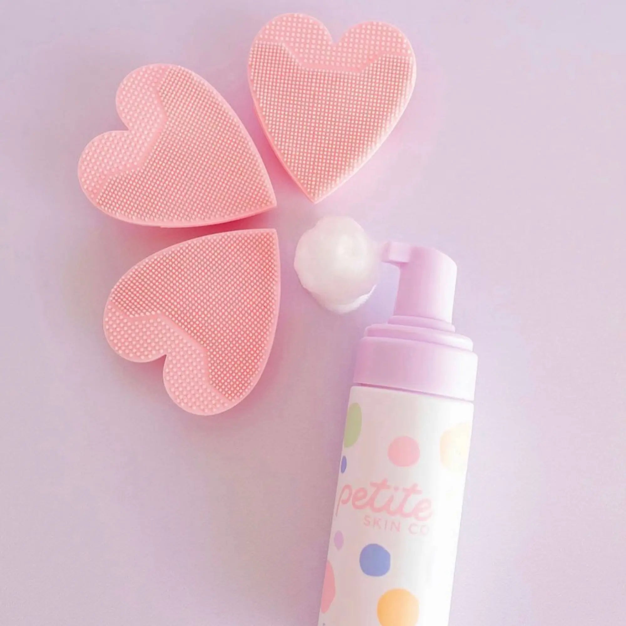 Three pink Heart Shaped Skin Buffers displayed next to a pump bottle of Gentle Face Cleansing Foam by Petite Skin Co., Australian made natural skincare for 7 to 14 year olds. Good Skin Habits Start Early.