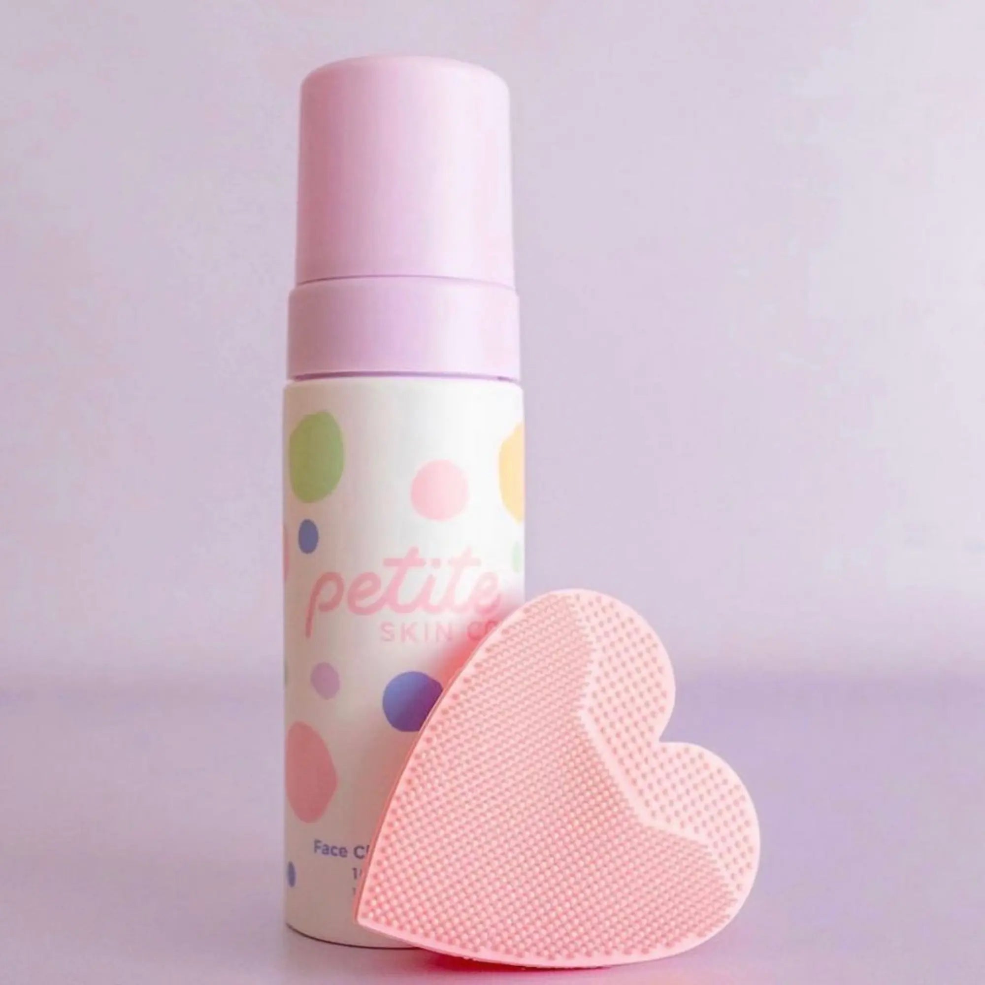 Pink Heart Shaped Skin Buffers next to a bottle of Petite Skin Co. Face Cleansing Foam, designed for Australian made natural skincare for 7 to 14 year olds with the tagline Good Skin Habits Start Early.
