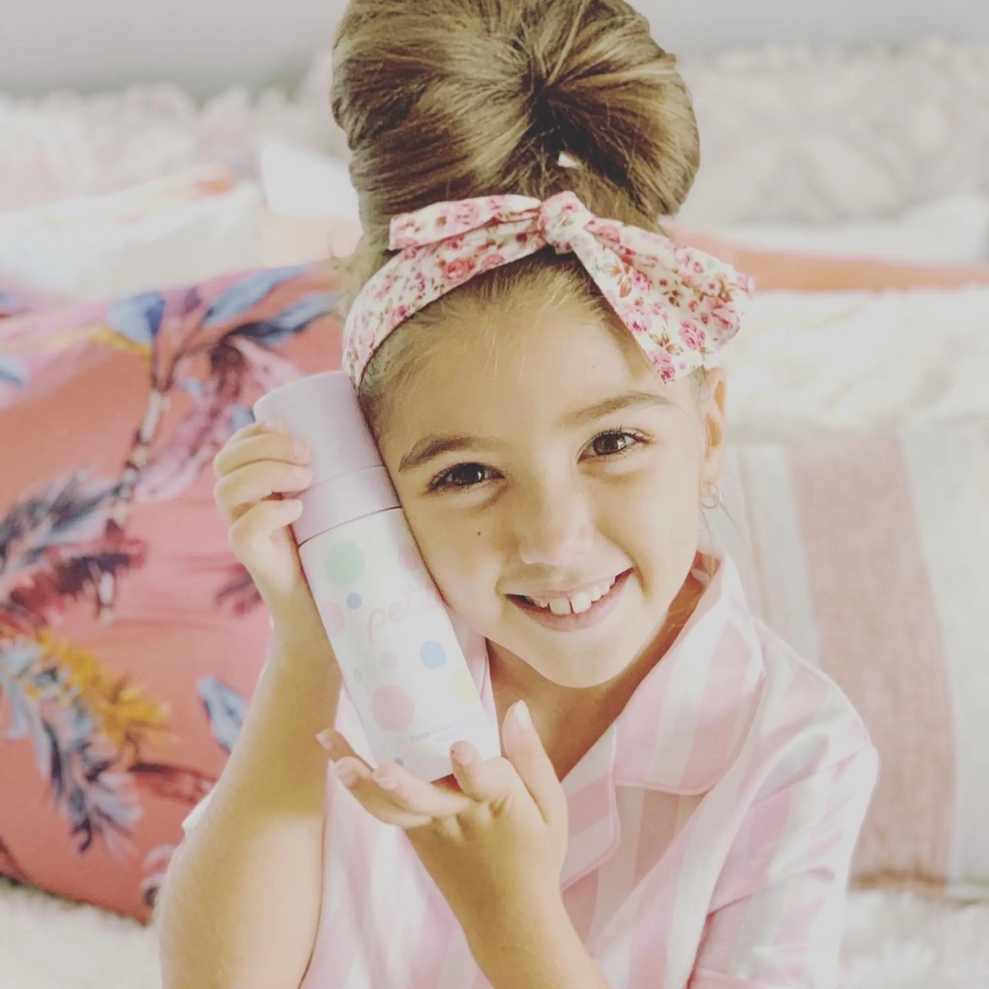 Young girl with a floral headband and hair in a bun, smiling and holding the Skin Bliss Kit, an Australian made natural skincare set for 7 to 14 year olds with gentle ingredients. Good Skin Habits Start Early.