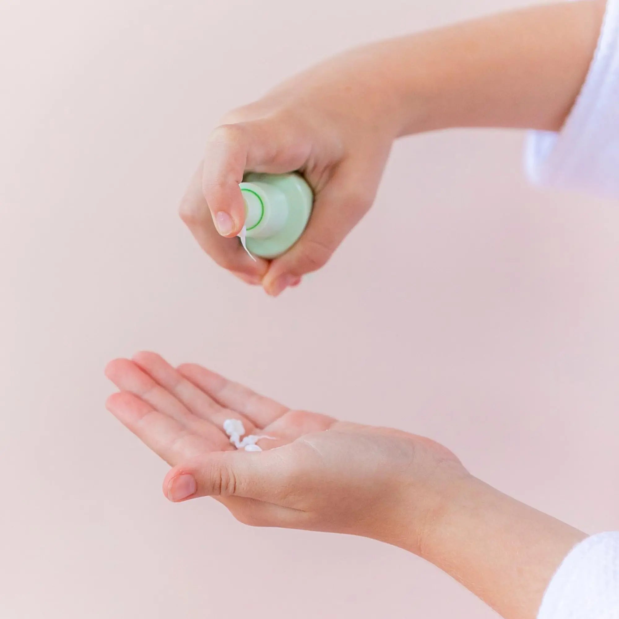 Child dispensing gentle cream from a small green bottle onto their palm as part of a daily skincare routine using the Skin Bliss Kit, Australian made, natural, designed for 7 to 14 year olds, promoting good skin habits early.