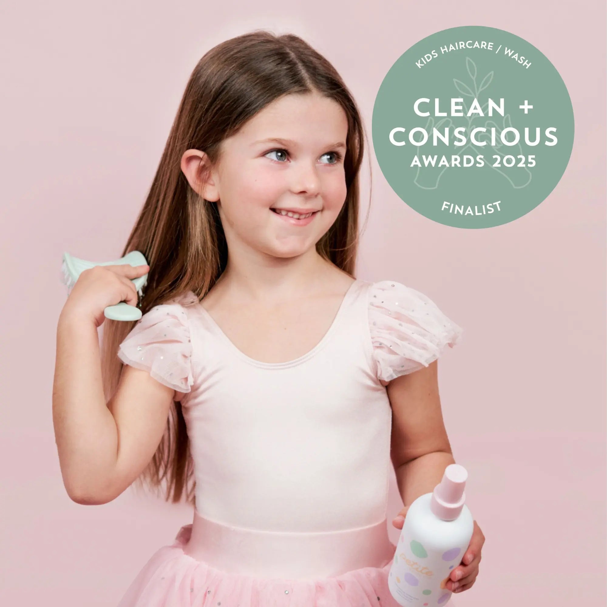 Young girl in a pink dress holding a bottle of Nourishing Detangler and brushing her long hair, showcasing Australian made gentle haircare for kids aged 7 to 14. Good Skin Habits Start Early.