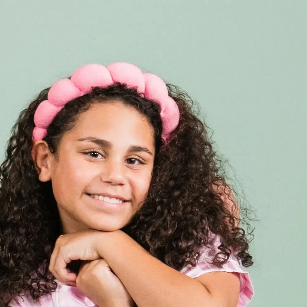 Smiling girl with curly hair wearing a soft pink headband, representing the gentle and natural Daily Refresh Set skincare routine designed for 7 to 14 year olds by Petite Skin Co., Australian made with a focus on good skin habits start early.