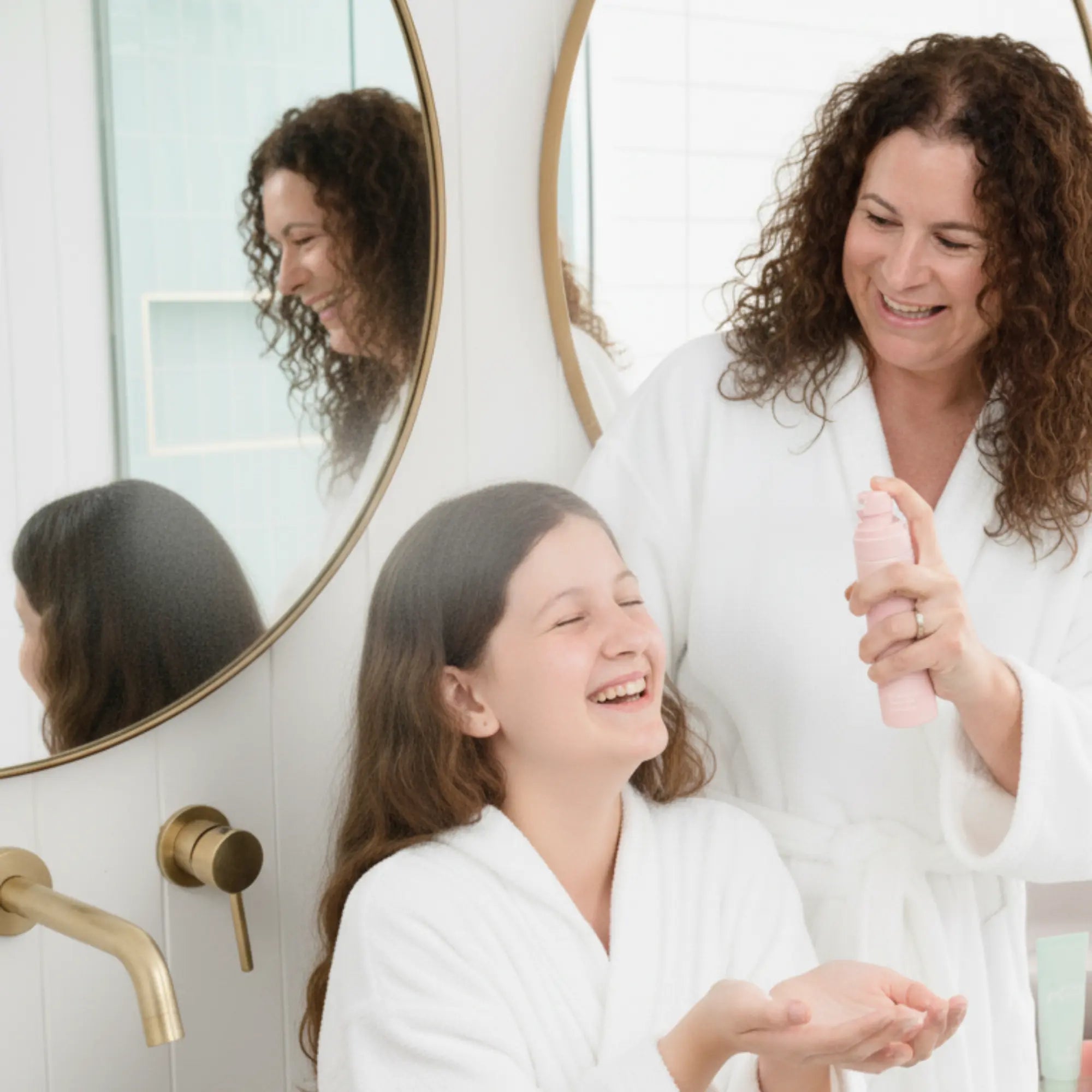 Mother and daughter in white robes smiling in a bathroom as the mother dispenses product from a pink bottle, promoting the Skin Bliss Kit with Australian made, natural skincare designed for 7 to 14 year olds – Good Skin Habits Start Early.