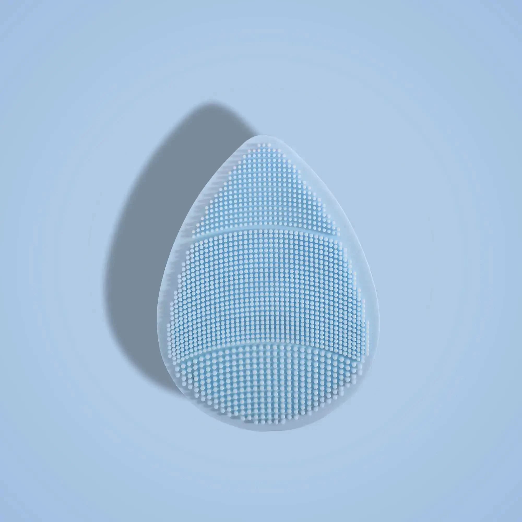 Teardrop-shaped skin buffer with a textured surface on a light blue background