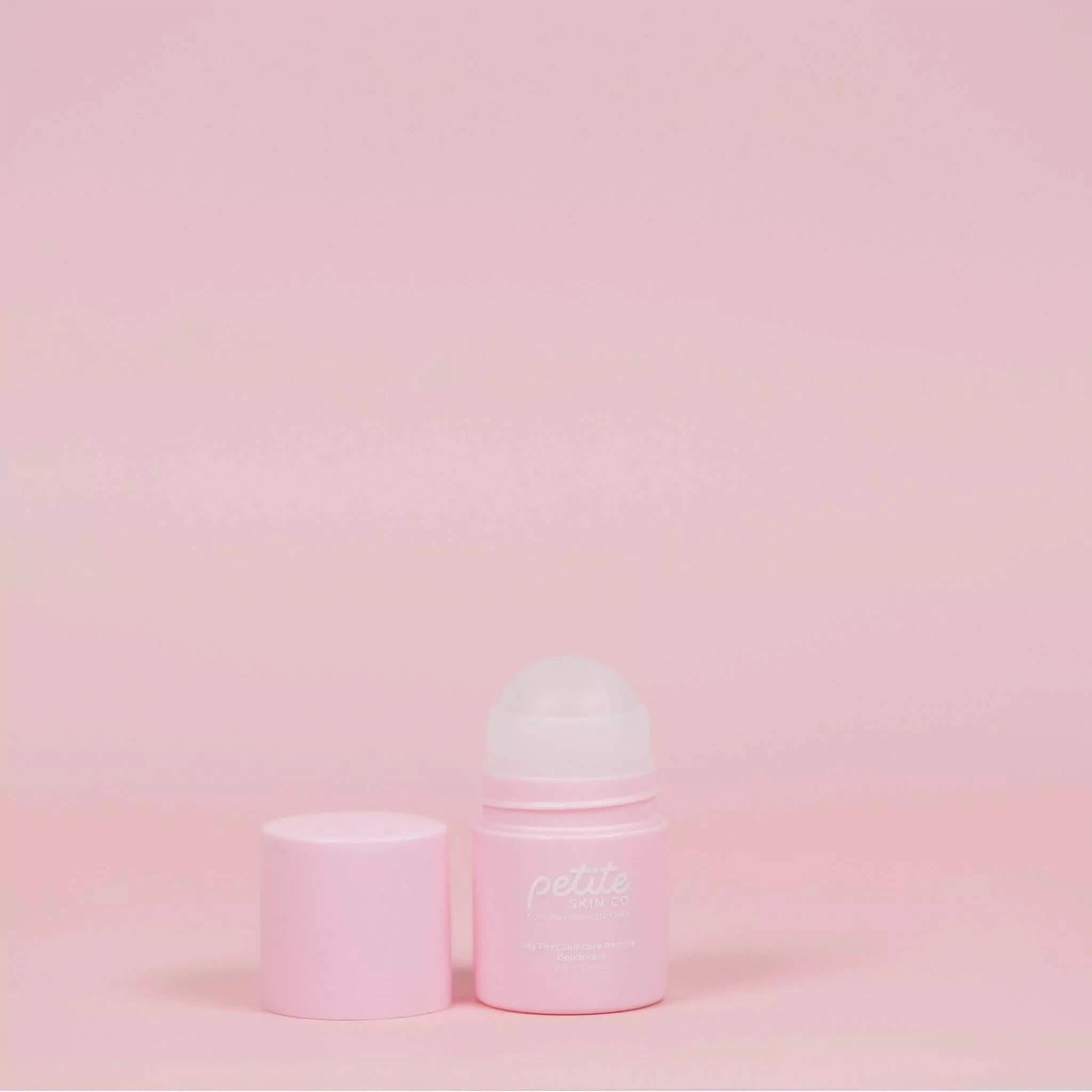 A pink roll-on deodorant bottle and lid against a pink background, labeled with 'Petite Skin Co.'
