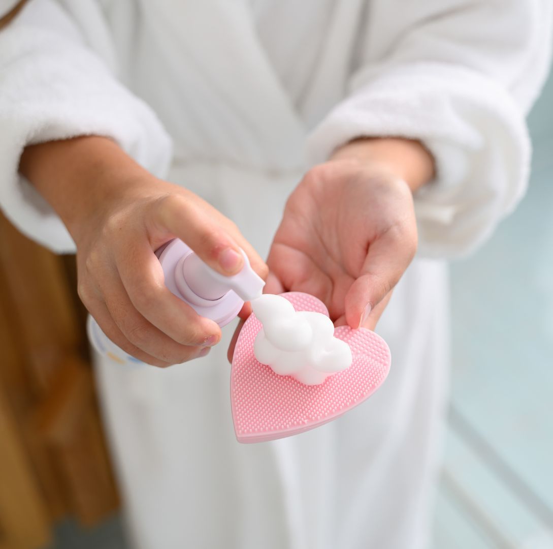 girl pumping white petite skin co foam onto pink heart skin buffer