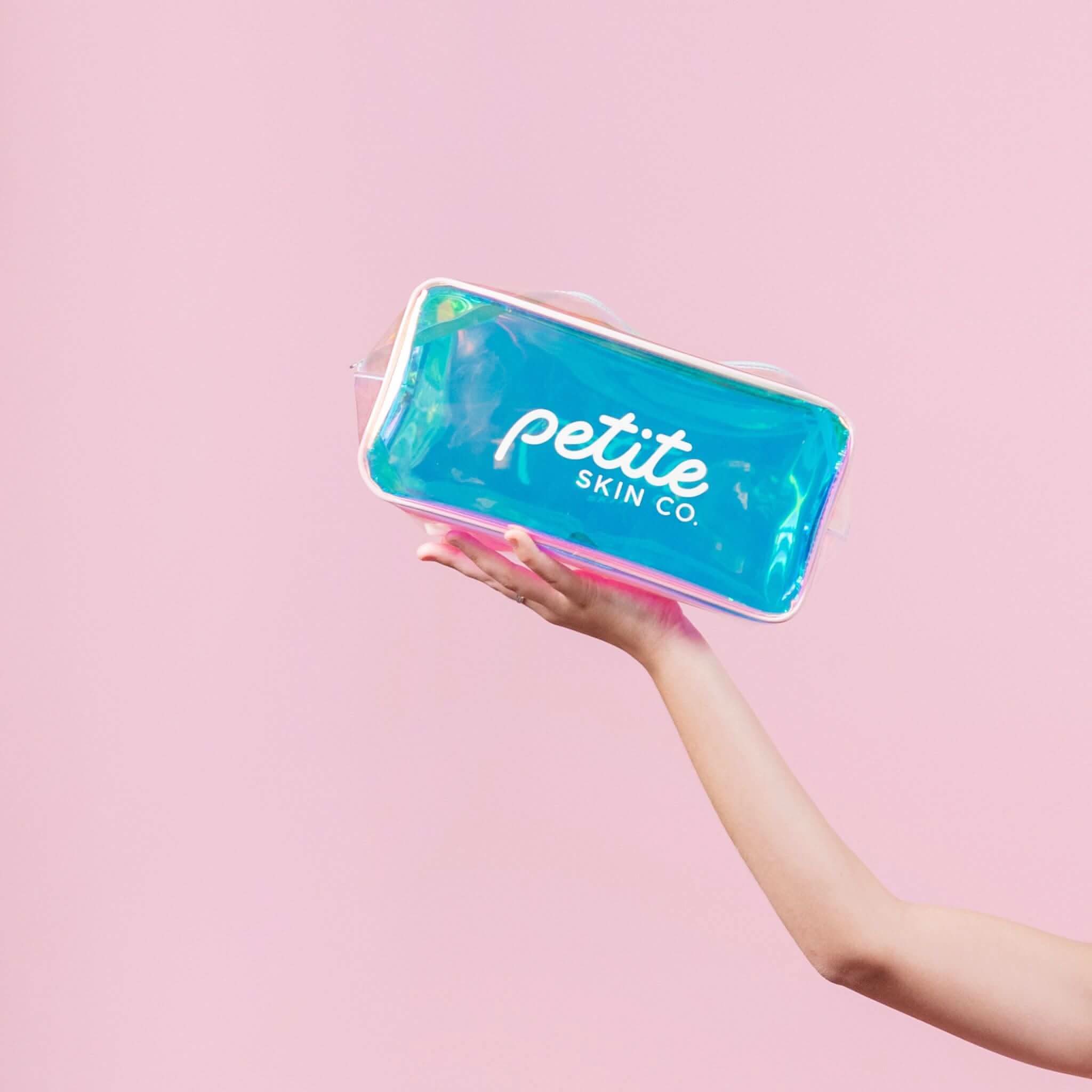 Hand holding a blue Holographic Skincare Bag with Petite Skin Co. logo against a pink background, Australian made and designed for gentle skincare routines for 7 to 14 year olds. Good Skin Habits Start Early.