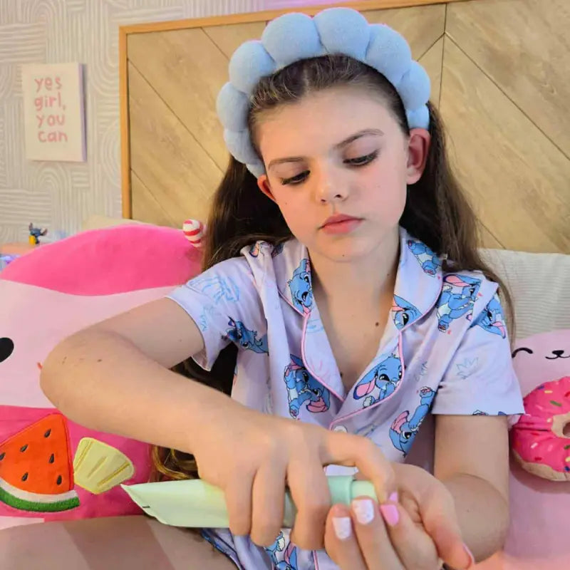 Young girl in pajamas sitting on a bed with colorful pillows.
