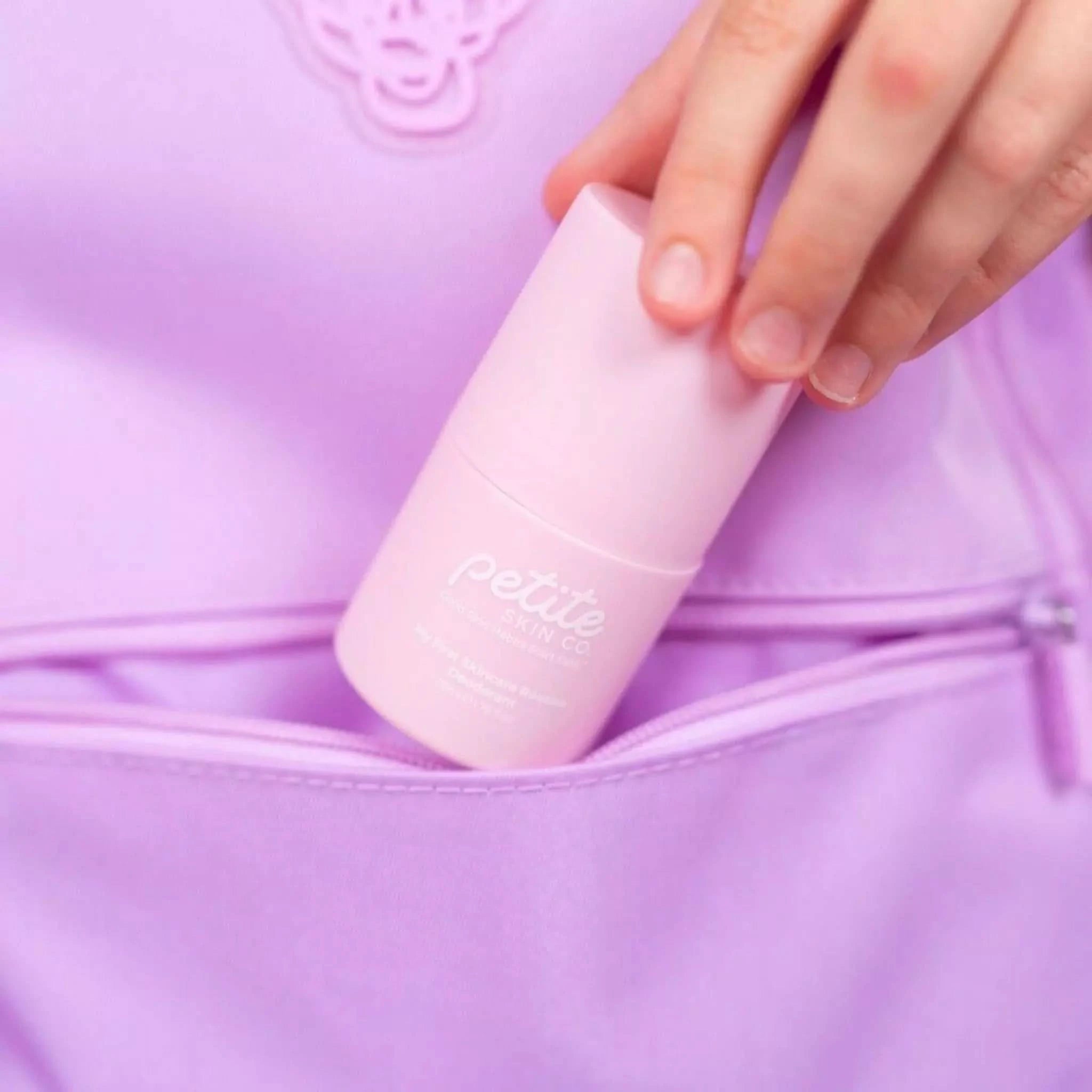 Hand placing a pink Petite Skin Co. Deodorant into a lavender backpack pocket, showcasing Australian made natural skincare designed for sensitive young skin aged 7 to 14, promoting good skin habits.
