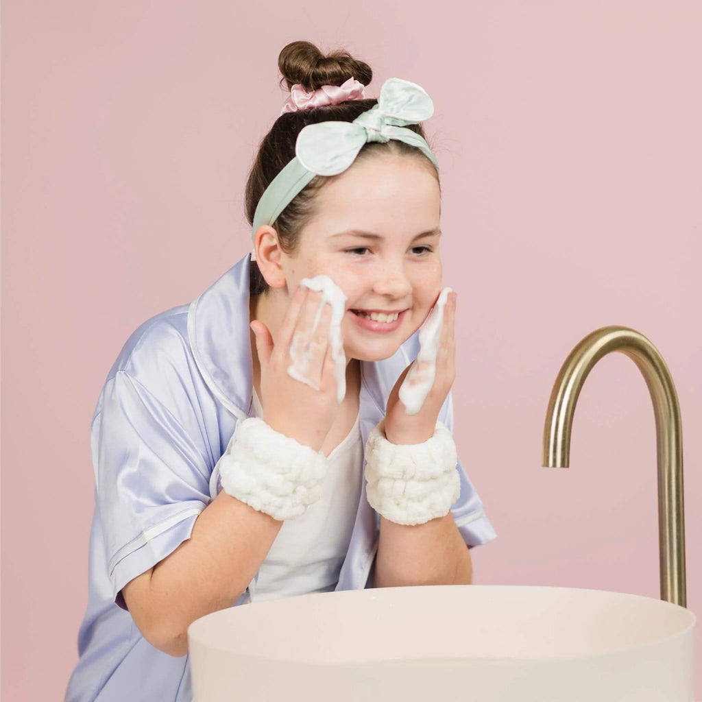 12 year old girl washing face with face cleanser wearing headband and scrunchie with Petite Skin Co. Dry Cuffs on the wrists to stop water dripping down the arms.