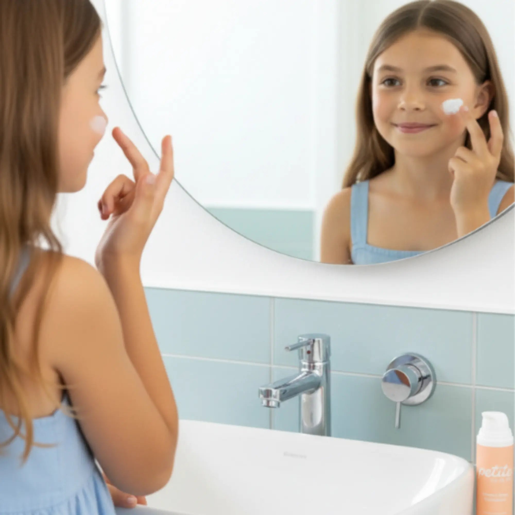 10 year old girl applying petite skin co spf50 face sunscreen to her face in front of a bathroom mirror.