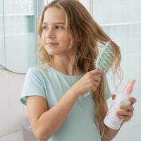Young girl using the Tangle-Free Duo nourishing detangler spray and dual-bristle brush to gently detangle her hair, promoting good hair care habits early, Australian made.