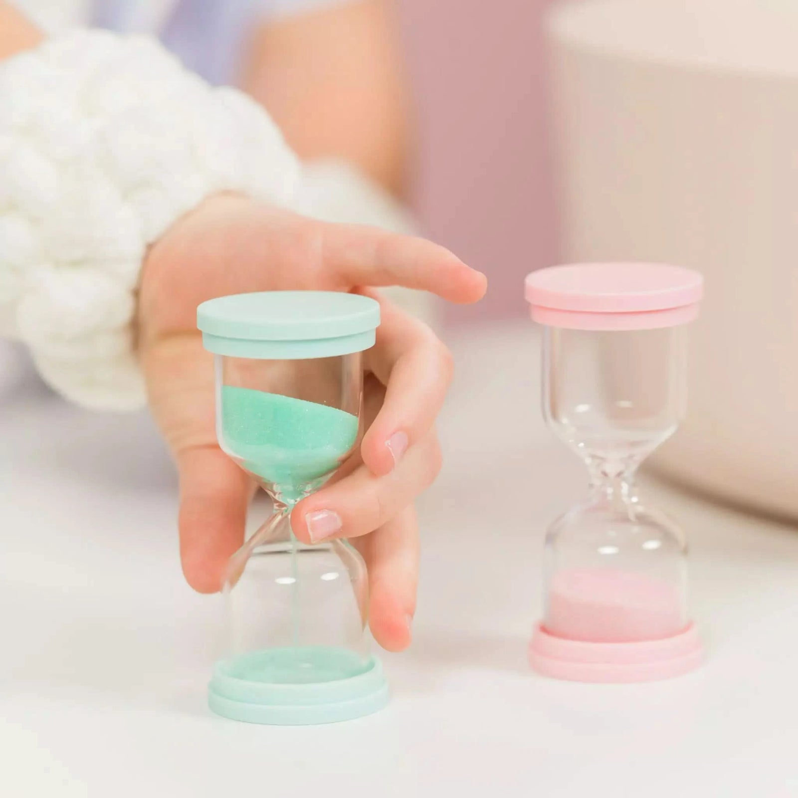 Two Australian made 60 Second Skincare Timer sandglasses in pastel pink and mint, designed to encourage good skin habits and gentle cleansing for 7 to 14 year olds.
