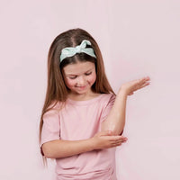 Young girl with long hair wearing a pink shirt and light green headband applying Body Cream to her elbow, showcasing Australian made, natural skincare for 7 to 14 year olds with the tagline Good Skin Habits Start Early.