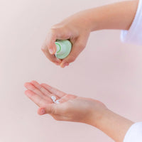 Child dispensing gentle cream from a small green bottle onto their palm as part of a daily skincare routine using the Skin Bliss Kit, Australian made, natural, designed for 7 to 14 year olds, promoting good skin habits early.