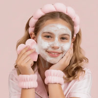 A smiling pre-teen girl with a pink headband and wristbands gently cleansing her face with foaming cleanser, demonstrating a gentle skincare routine for young, sensitive skin.