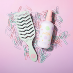 Hairbrush and bottle of detangler on a pink background