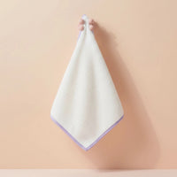 Hand holding a soft white Face Towel with light purple edging against a neutral background, Australian made for gentle skincare and hygiene for 7 to 14 year olds. Good Skin Habits Start Early.