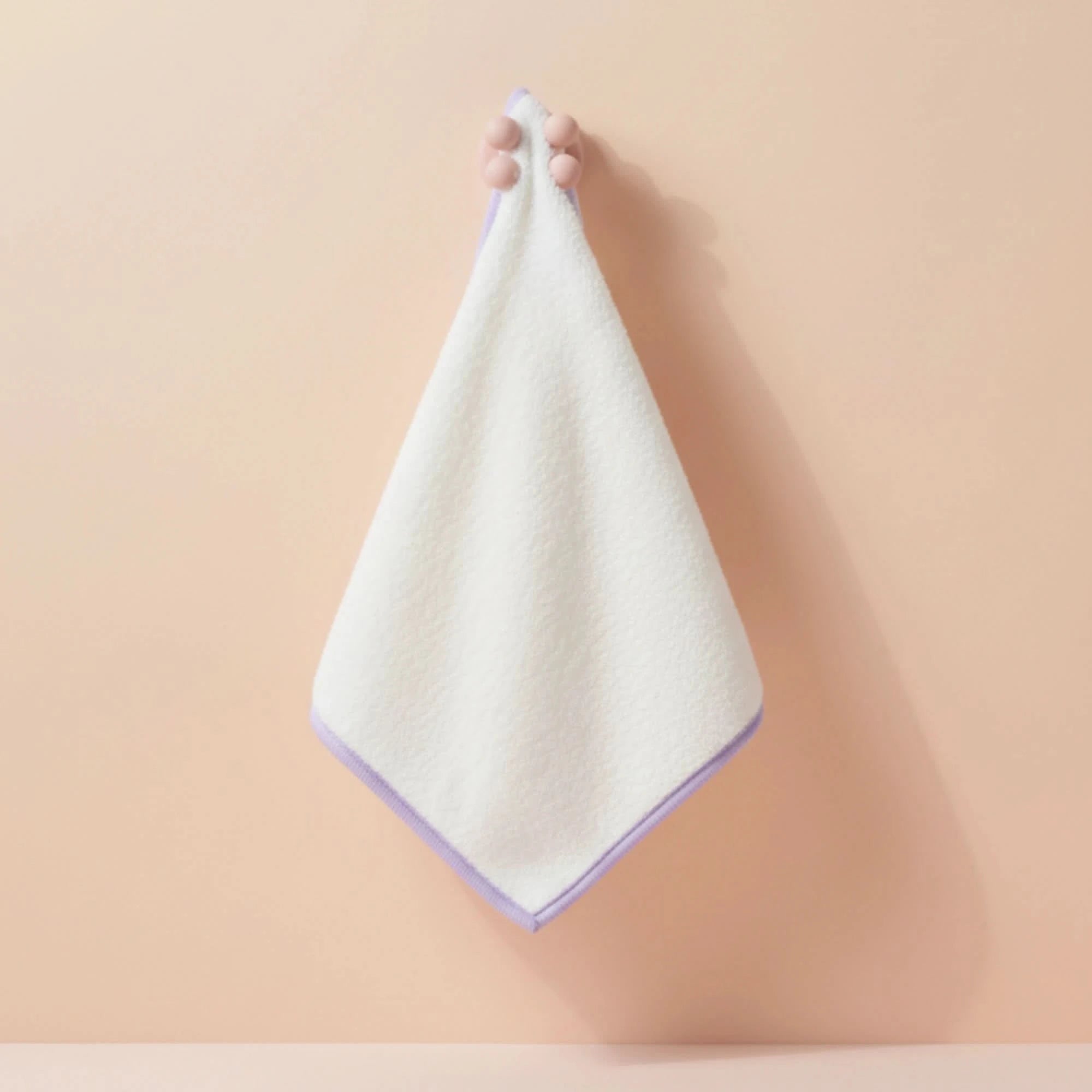 Hand holding a soft white Face Towel with light purple edging against a neutral background, Australian made for gentle skincare and hygiene for 7 to 14 year olds. Good Skin Habits Start Early.