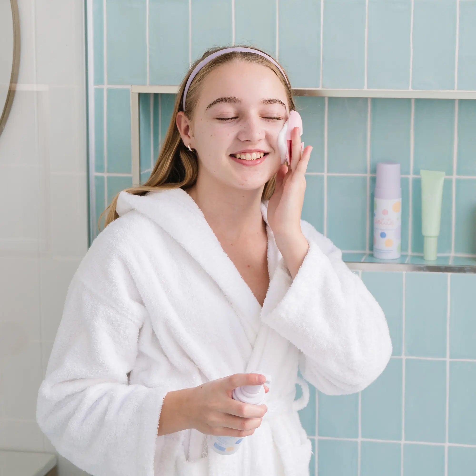 Young girl in a white robe using Teardrop Shape Skin Buffers to gently cleanse her face with a smile, promoting good skin habits early with Australian made skincare for ages 7 to 14.