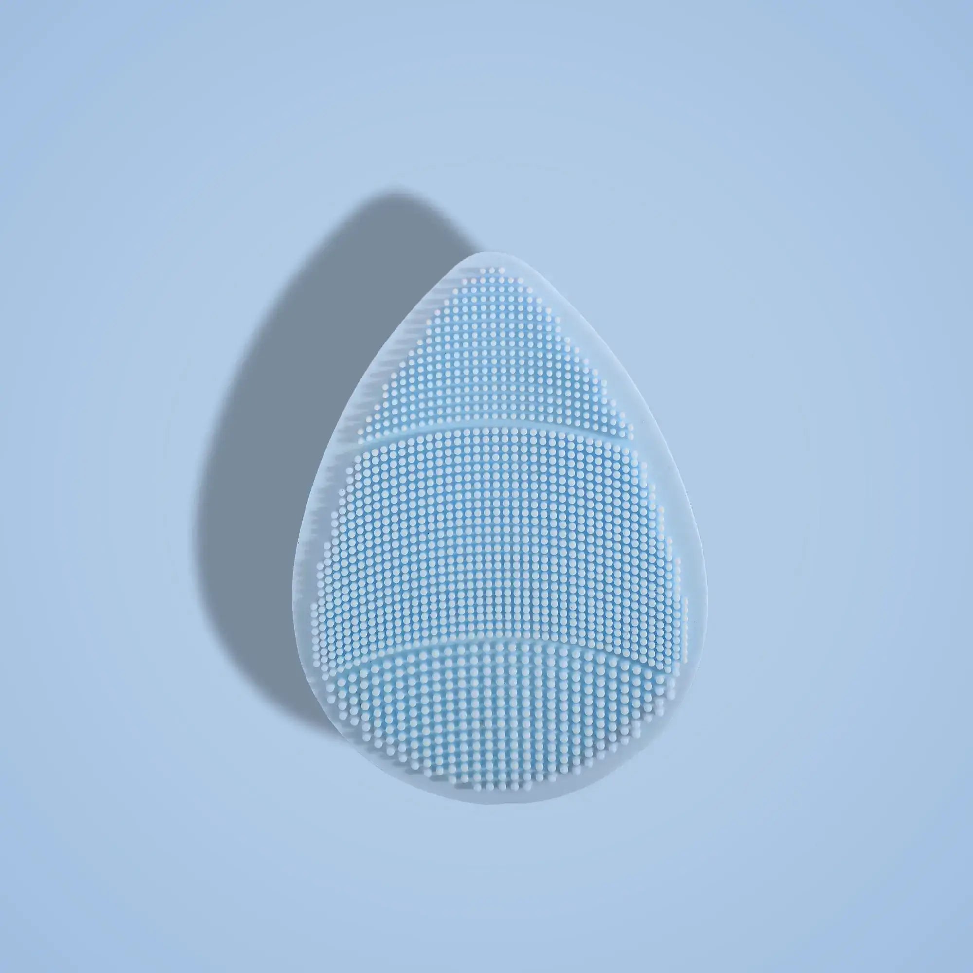 Teardrop-shaped skin buffer with a textured surface on a light blue background