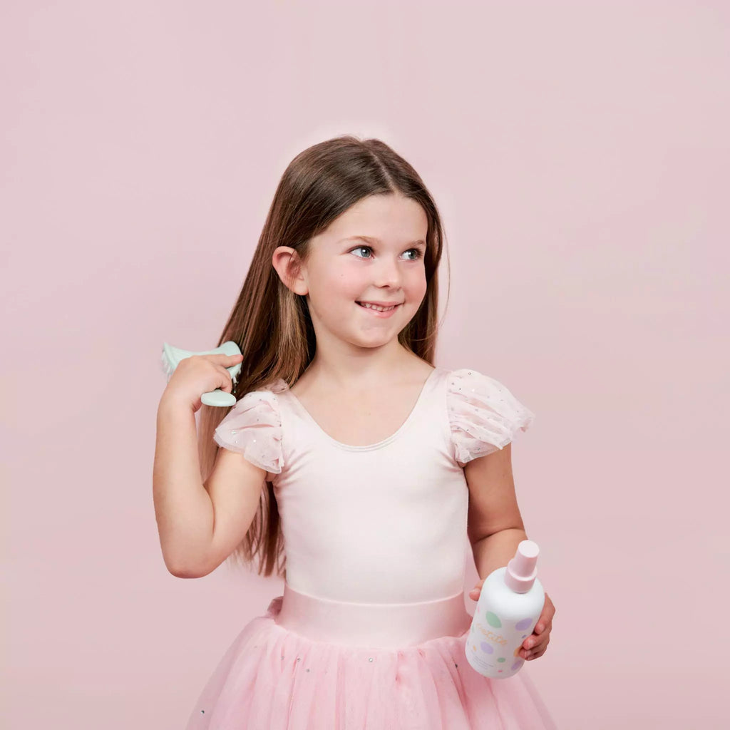 8 year old girl brushing her hair with the Petite Skin Co. detangling brush with her right hand and holding the Petite Skin Co. Detangler in the other hand