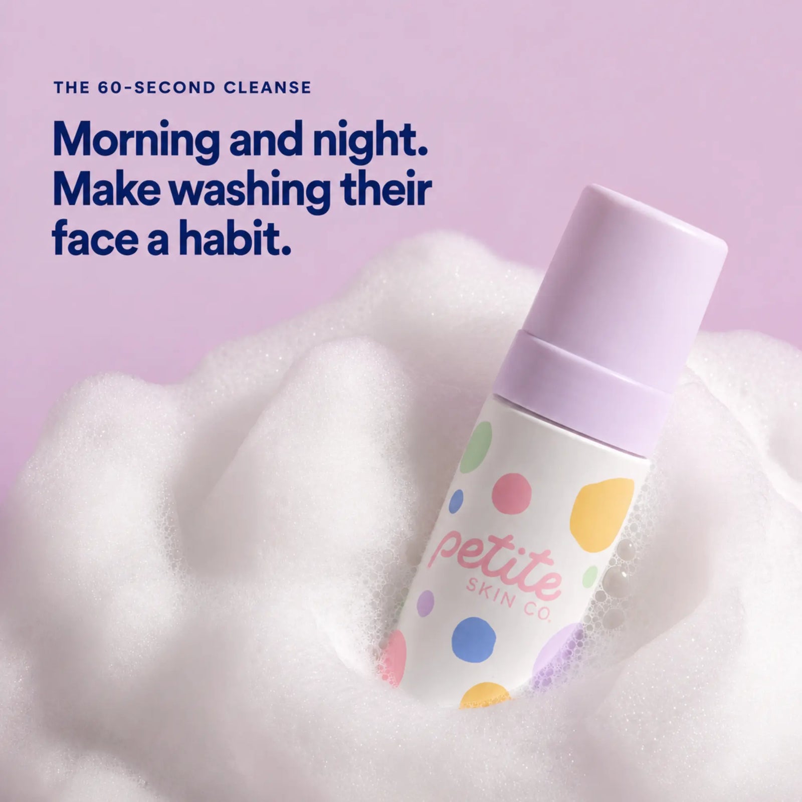 A bottle of Petite Skin Co. foaming cleanser with a lavender cap and a white body decorated with colorful polka dots, emerging from white foam against a soft lavender background with promotional text.