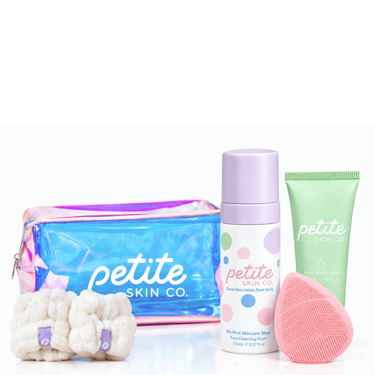 Petite Skin Co. skincare gift set featuring a holographic zippered pouch, a white foaming cleanser bottle with a lavender cap, a mint green body wash tube, and a pink silicone sponge, arranged on a white background.