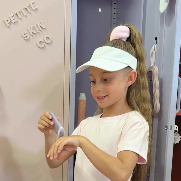 Young girl with a pale visor applies sunscreen from a tube onto her hand using the Sunscreen Applicator Brush, promoting good skin habits early with Australian made gentle skincare for ages 7 to 14.
