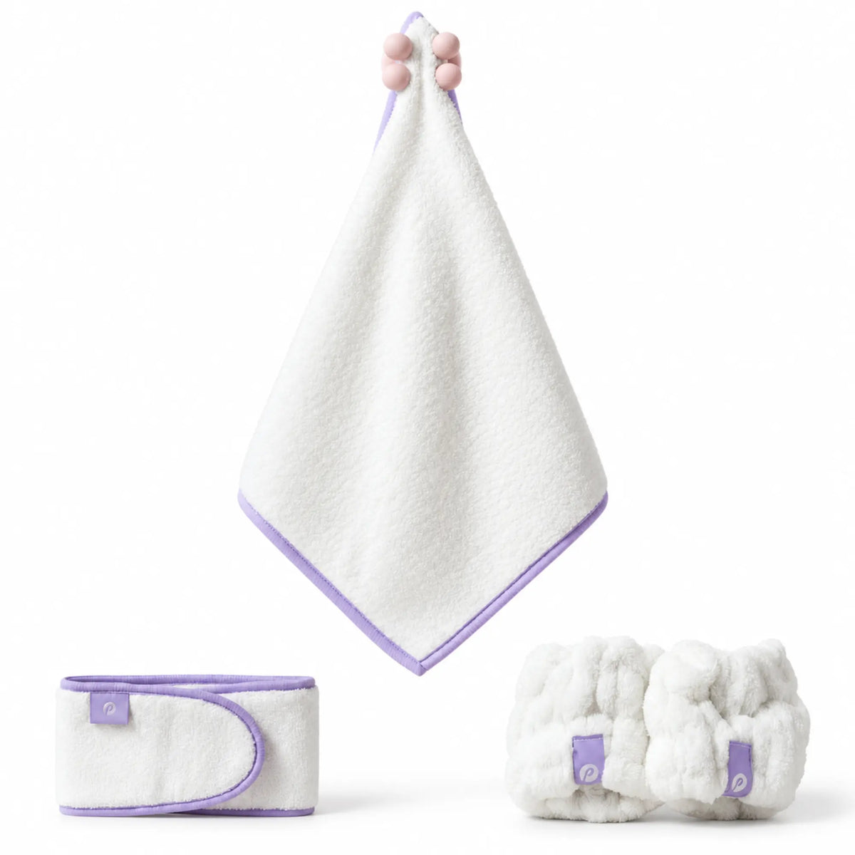 A white baby towel set with light purple trim, including a hanging towel held by a hand, a folded wrap, and a rolled bundle of plush washcloths, on a white background.