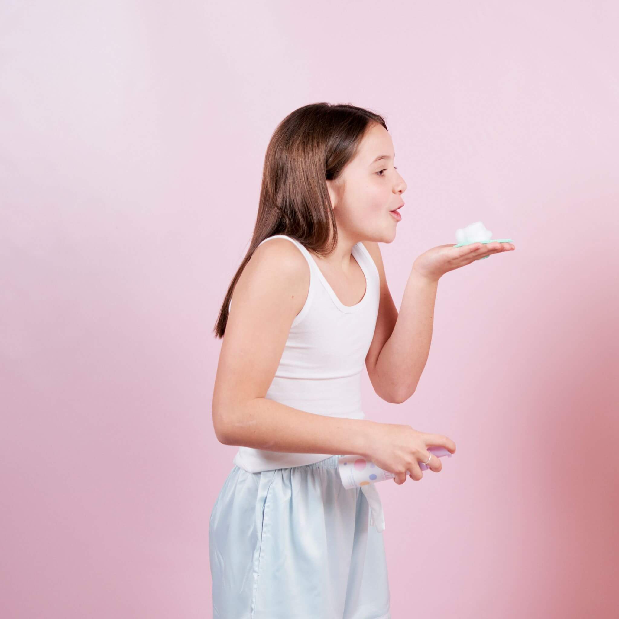 girl blowing face cleansing foam off hand on pink background