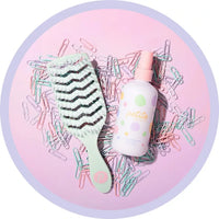 Pastel-colored hairbrush and hair tie on a pink background with paper clips.