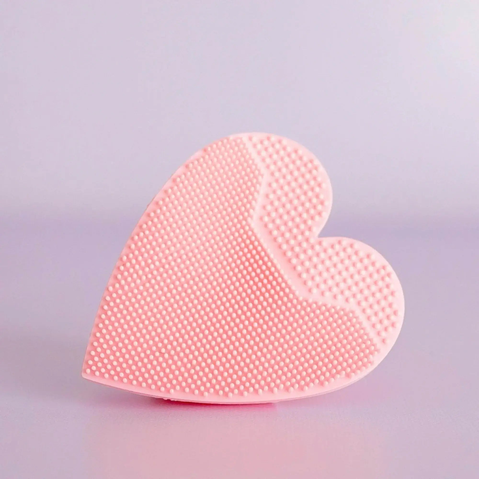 Heart-shaped pink silicone scrubber on a light purple background