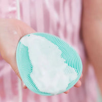 Hand holding a mint green Body Buffer with soft silicone bristles covered in foamy body wash, designed for gentle Australian made skincare for children aged 7 to 14. Good Skin Habits Start Early.