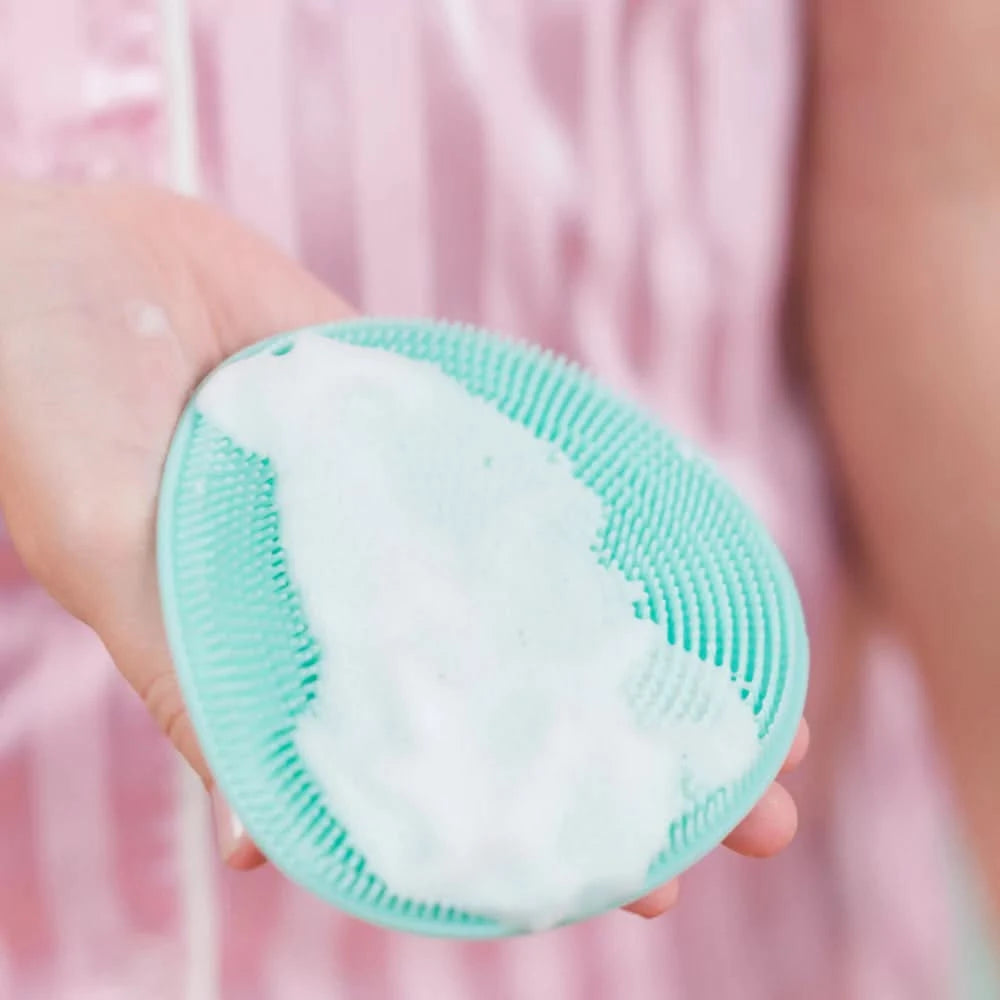 Hand holding a mint green Body Buffer with soft silicone bristles covered in foamy body wash, designed for gentle Australian made skincare for children aged 7 to 14. Good Skin Habits Start Early.