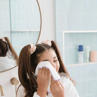 Woman cleaning her face with a white cloth in a bathroom.