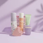Set of skincare products including a clenaser, sunscreen, moisturisrer and heart buffer on a light purple background.