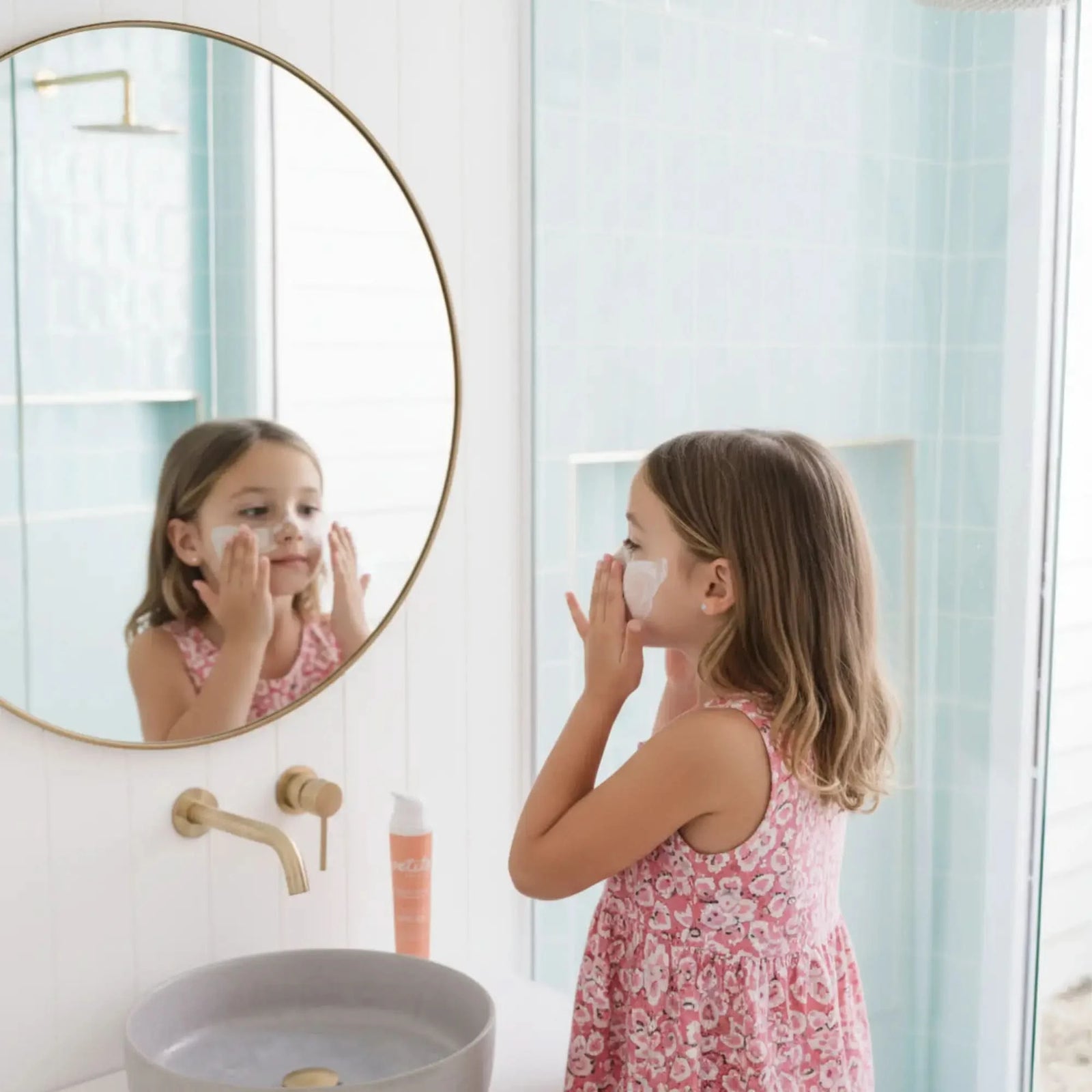 Young girl applying SPF50 Face Sunscreen - NEW FORMULATION in front of bathroom mirror, demonstrating gentle, Australian made skincare for 7 to 14 year olds. Good Skin Habits Start Early.
